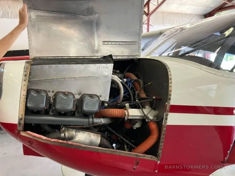 A close-up view of the open engine cowling of a red and white aircraft, revealing the engine components.