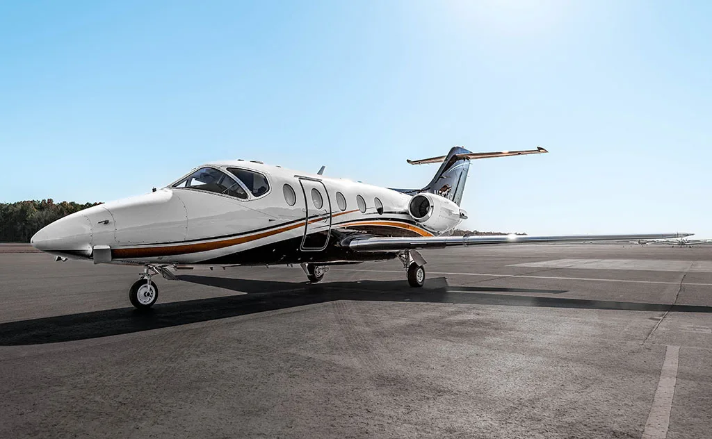 A white and black business jet with orange stripes is parked on an asphalt runway under a clear blue sky.