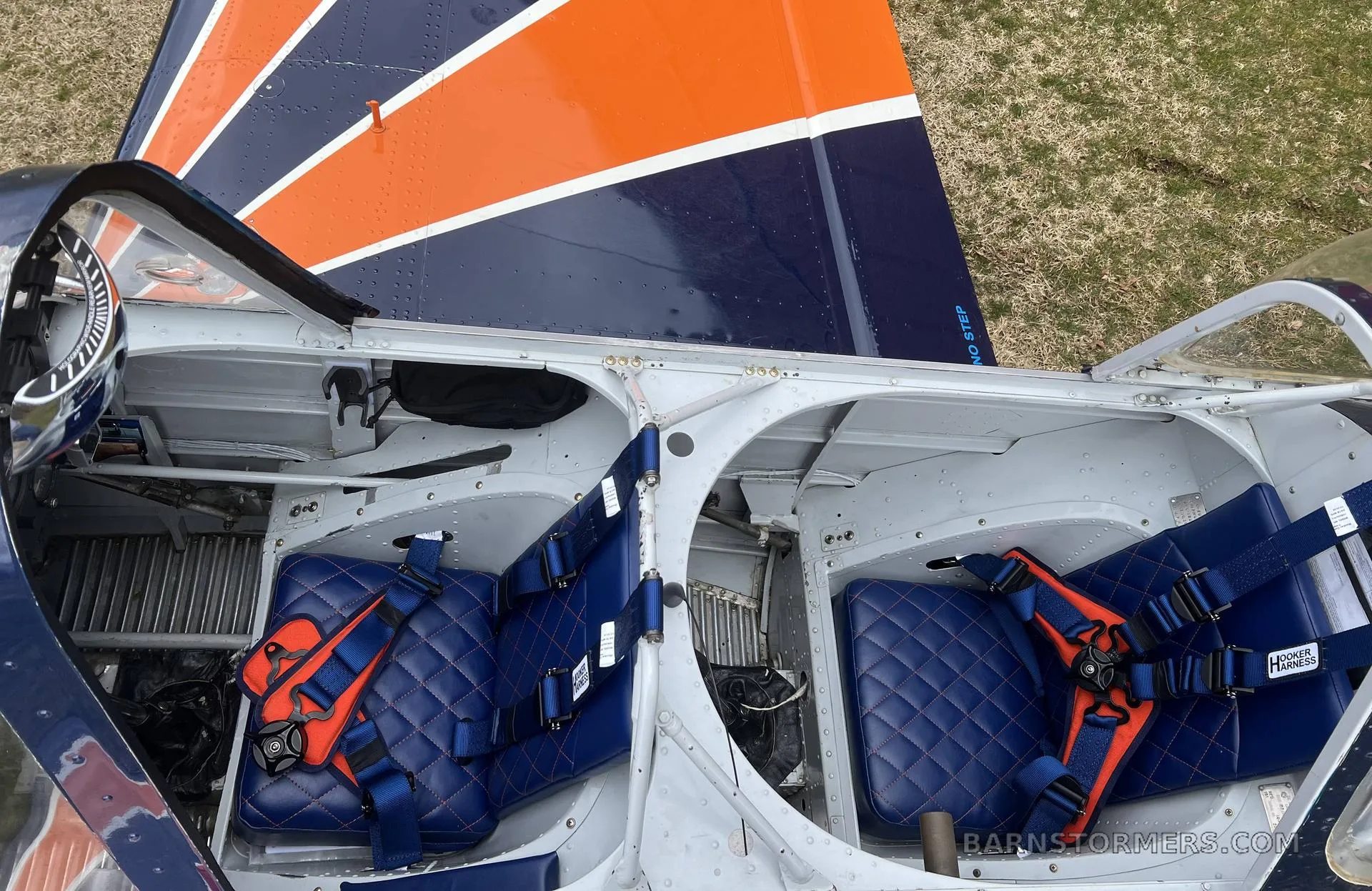 An overhead view of the aircraft's open cockpit showing two blue quilted seats with orange harnesses.