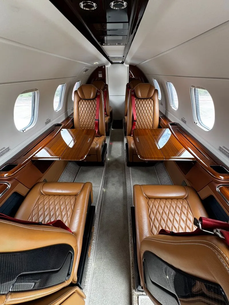 The luxurious interior of an aircraft cabin with quilted brown leather seats and polished wood tables.