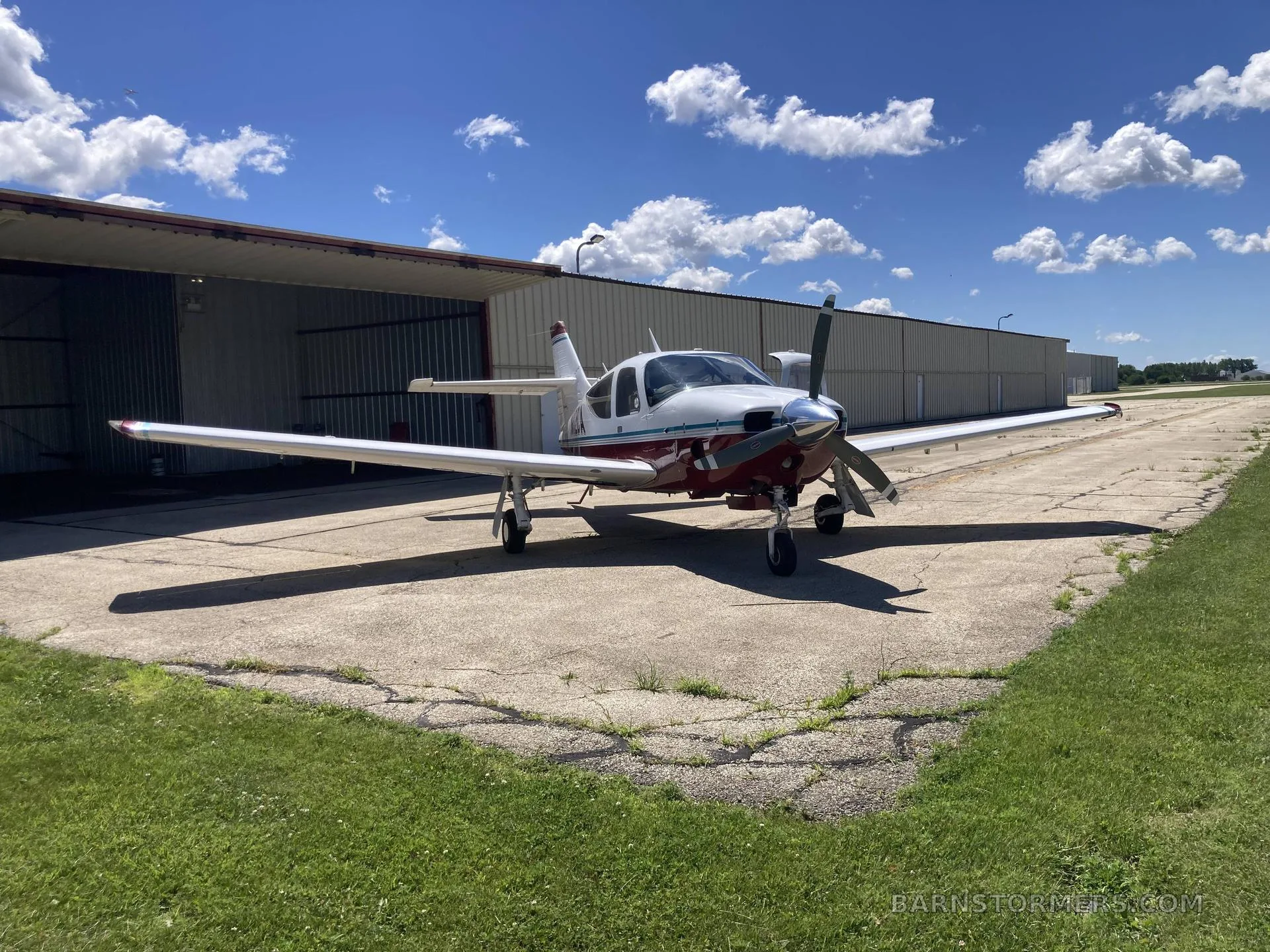 A white and red single-engine propeller aircraft (N112CA) parked on a concrete pad in front of an open hangar.