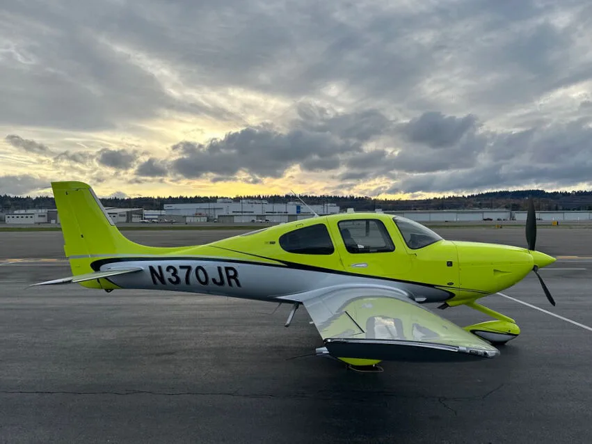 A side view of the bright yellow and silver Cirrus SR22 aircraft with registration N370JR parked on an airport tarmac.