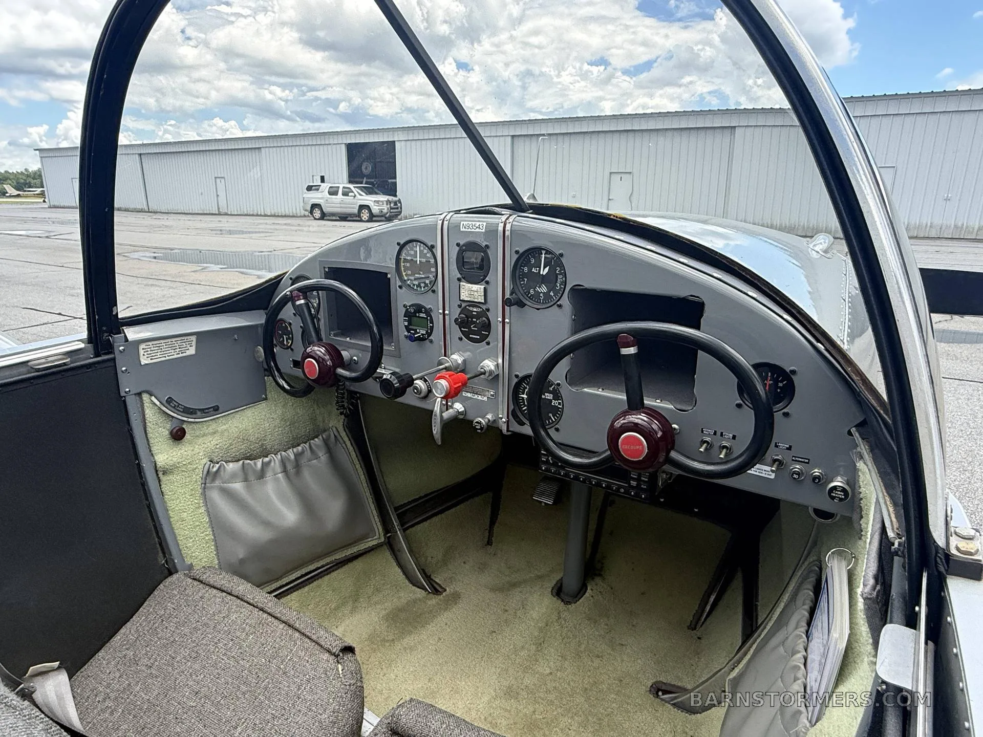 The interior of a vintage-style aircraft cockpit, showing the instrument panel, dual controls, and fabric seats.
