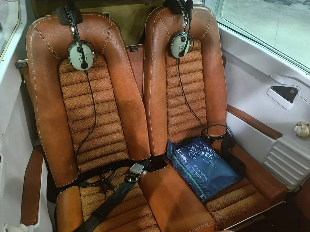 The two brown leather and fabric seats of the aircraft's cabin, with headsets hanging on them.