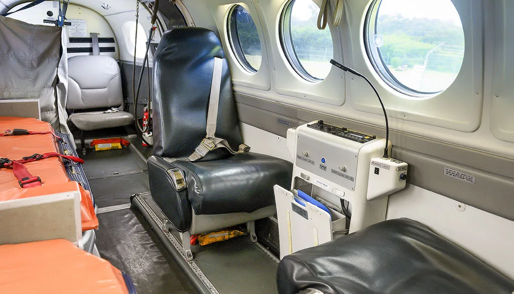 The interior of an air ambulance cabin, showing a black seat, an orange stretcher, and medical equipment.