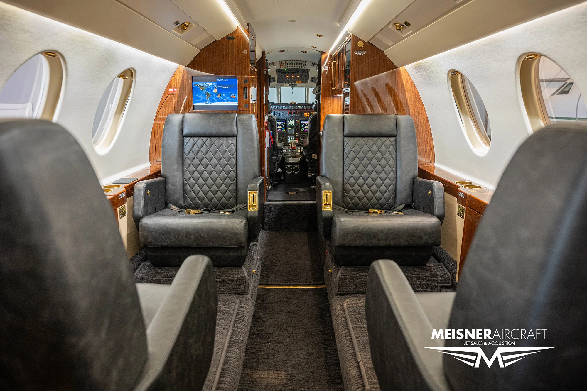 The luxurious cabin interior of a Dassault Falcon 900EX business jet with dark quilted leather seats and wood paneling.