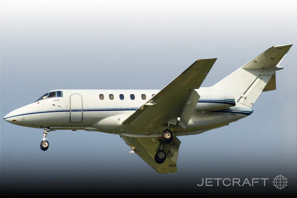 A white business jet with blue accent stripes, landing gear extended, against a grey sky.