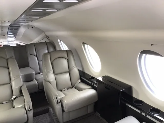 A side view of the business jet's cabin shows grey leather seats, oval windows, and a small cabinet.