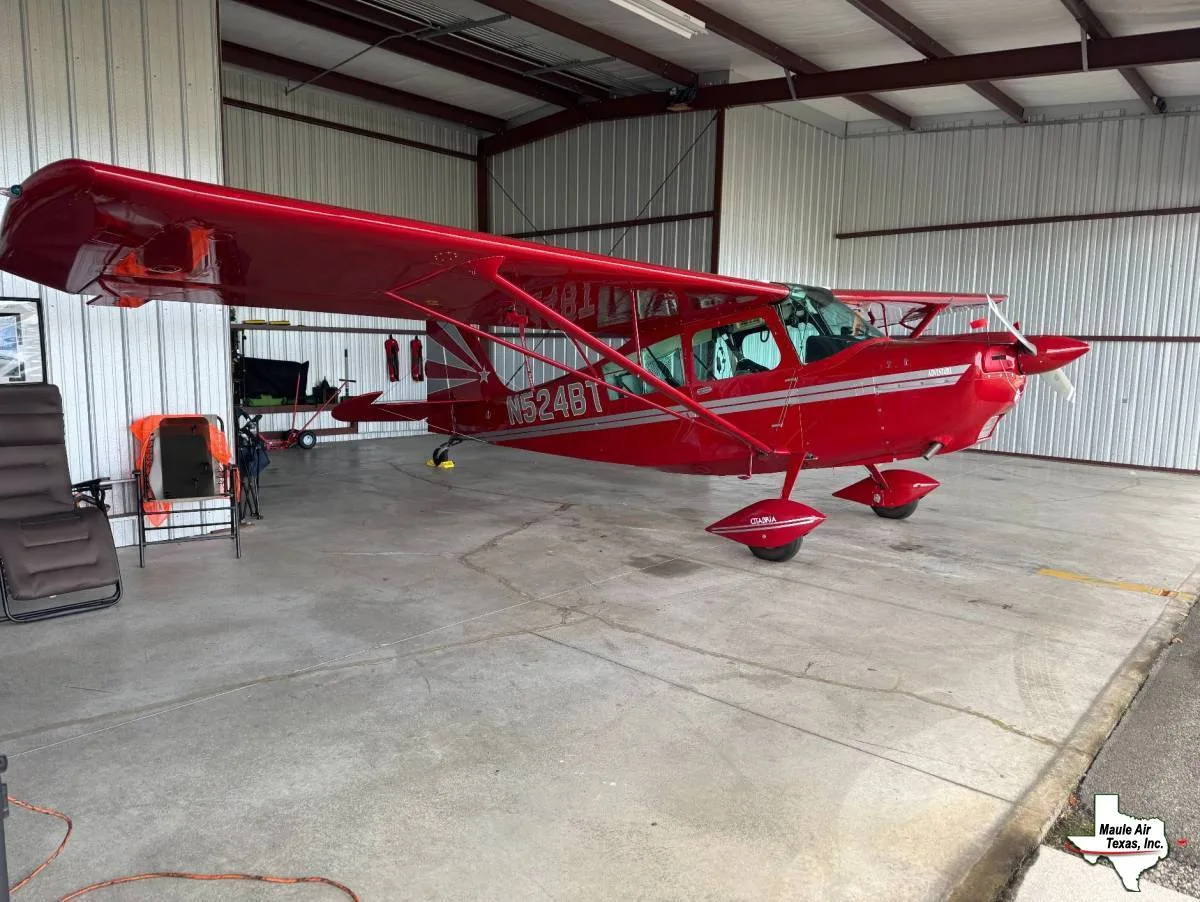 A red Maule aircraft with silver stripes and registration N524BT is parked inside a hangar.