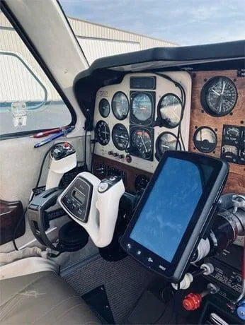 Close-up of the aircraft cockpit with analog gauges, a yoke, and a modern tablet mounted on the panel.