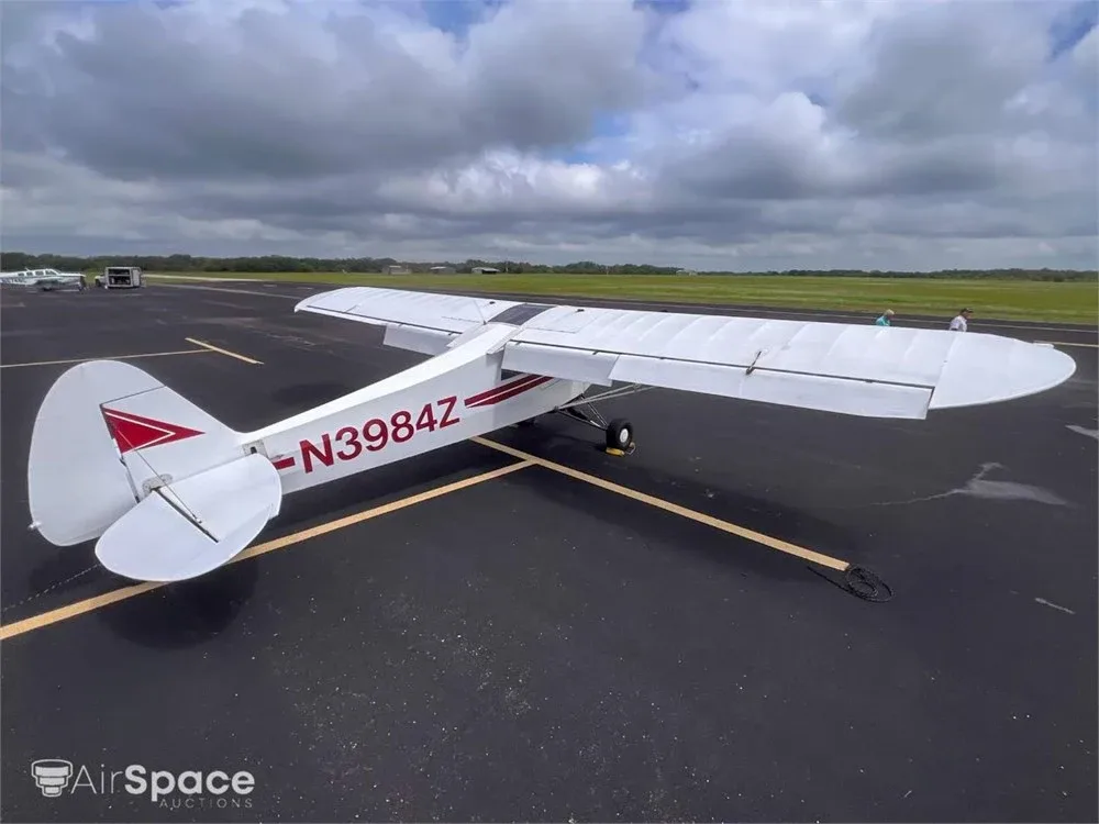 An aerial view of the white high-wing aircraft N3984Z with red stripes, parked on an asphalt runway under a cloudy sky.