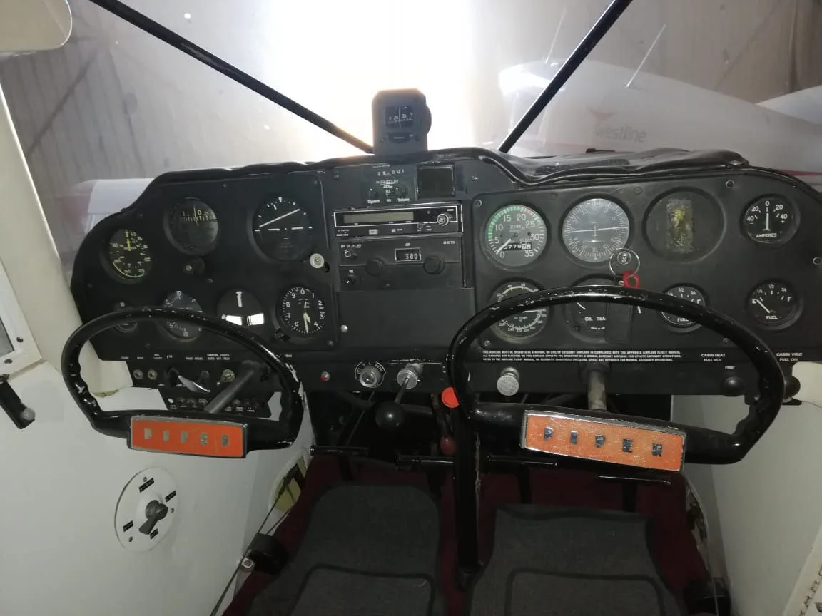 The cockpit of a Piper aircraft, showing a black instrument panel with gauges and two control yokes.