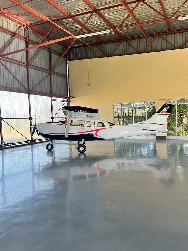 A side view of a white and black Cessna aircraft with red stripes is parked inside a hangar.
