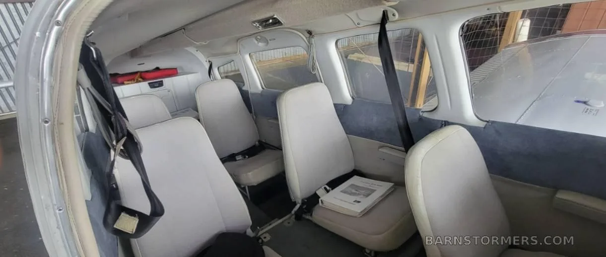 The interior cabin of a Piper Cherokee Six 300, showing four light-colored passenger seats with seatbelts and a book on one seat.