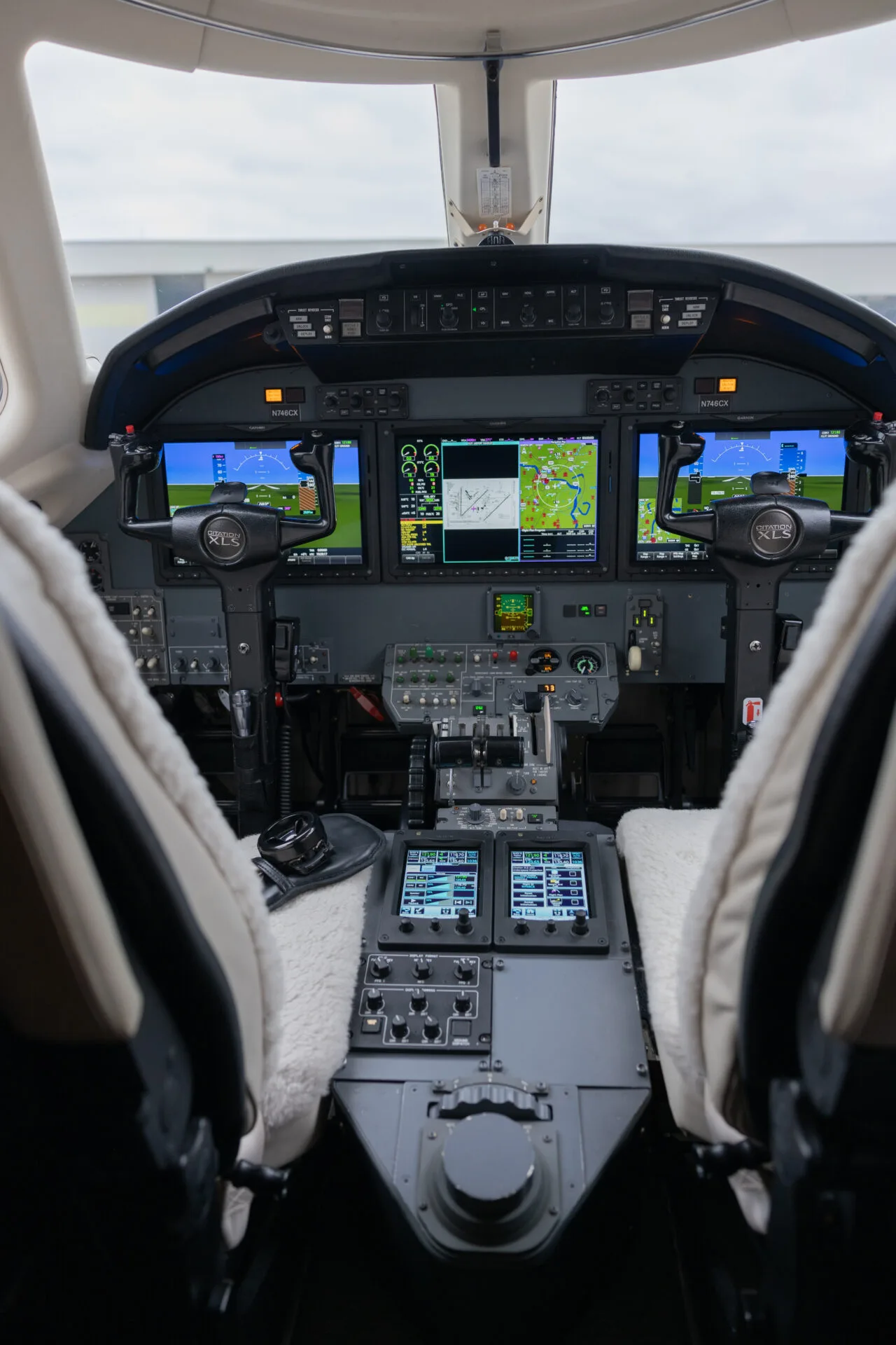 The cockpit of a private jet with multiple digital displays, control yokes, and a central throttle quadrant.