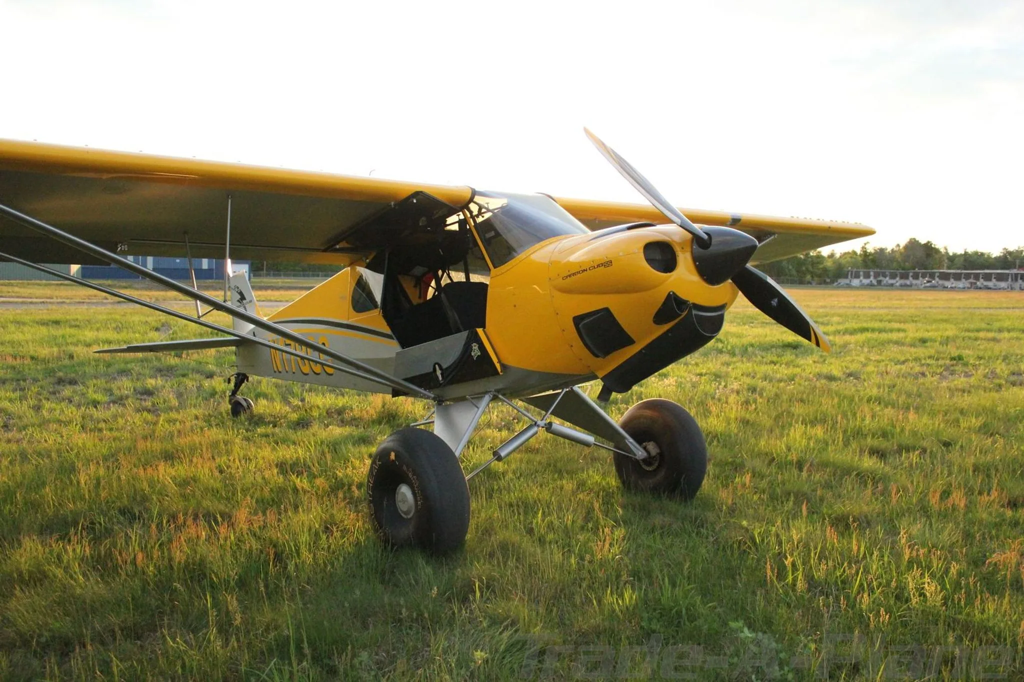 A yellow and grey Carbon Cub aircraft, N178CC, with large tundra tires, parked on a grassy field at sunset.