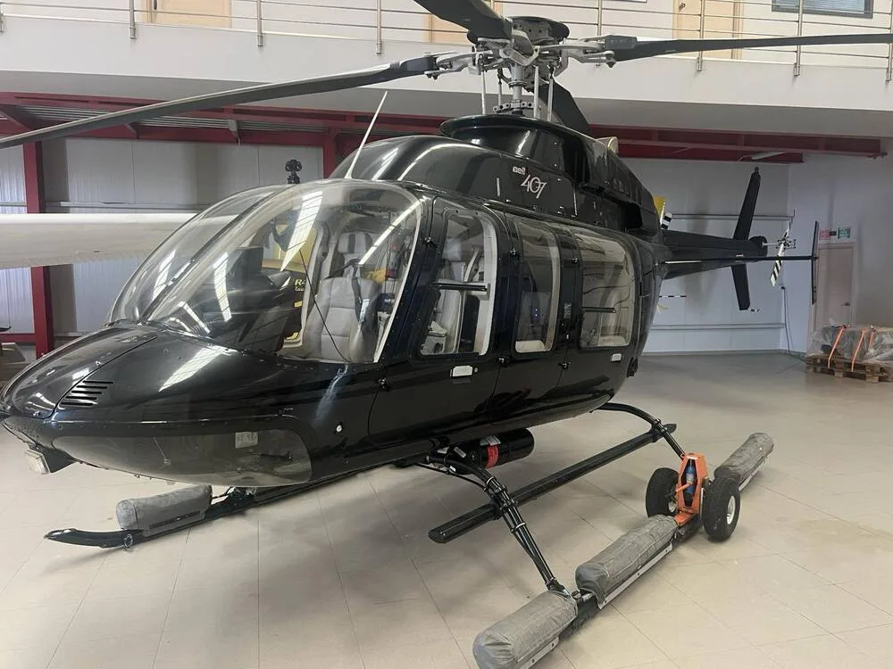 A black helicopter with skids and wheels on the ground inside a hangar.