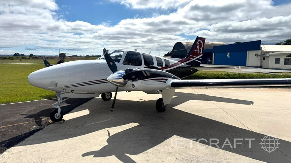 A white and black twin-engine propeller aircraft with red accents on the tail, parked on an asphalt ramp under a partly cloudy sky.