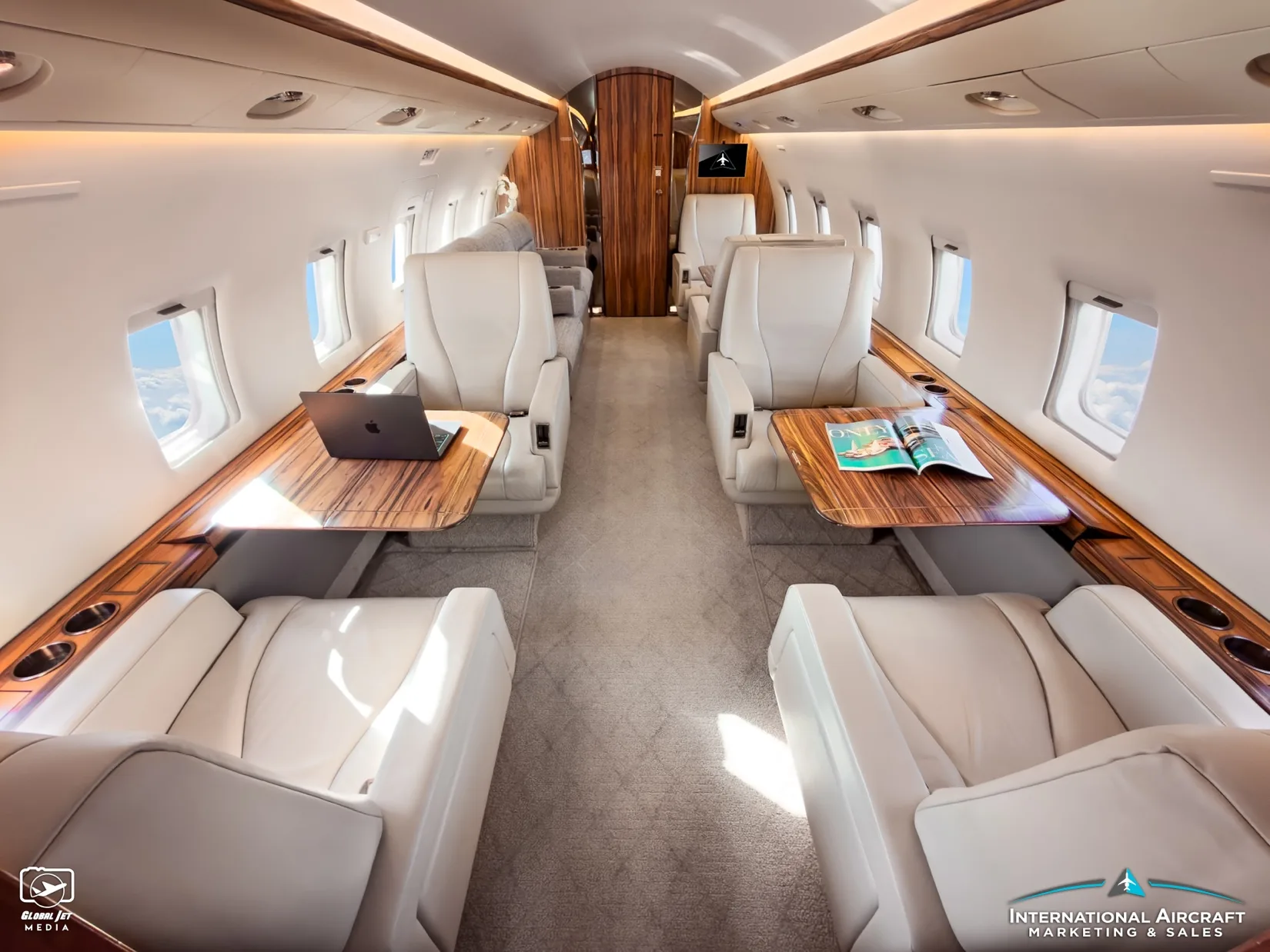 Cabin of the Bombardier Challenger with white leather seats and wood tables.