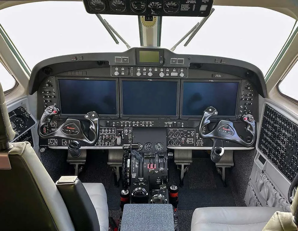 The cockpit of an aircraft featuring three large digital displays, dual control yokes, and a central console.