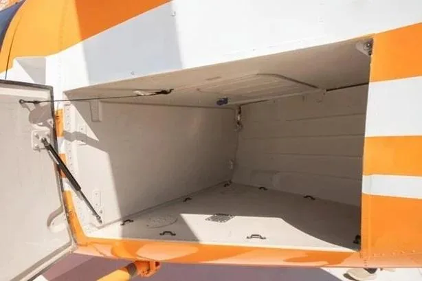 An open external baggage compartment on the side of an orange and white helicopter.