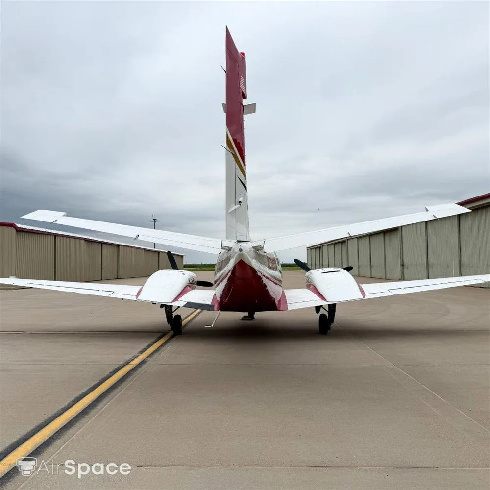 Rear view of a white and red Beechcraft Duke N2889W parked on a tarmac with hangars in the background.