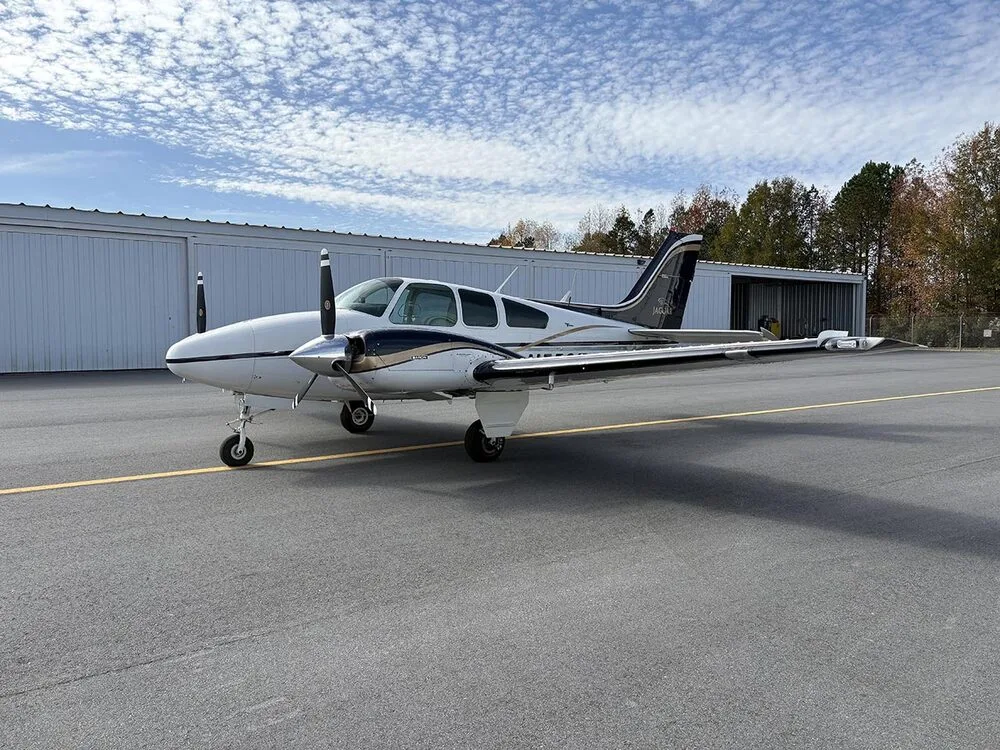 A white and dark blue twin-engine aircraft with registration N55SE is parked on the tarmac, viewed from a wider front-left angle.