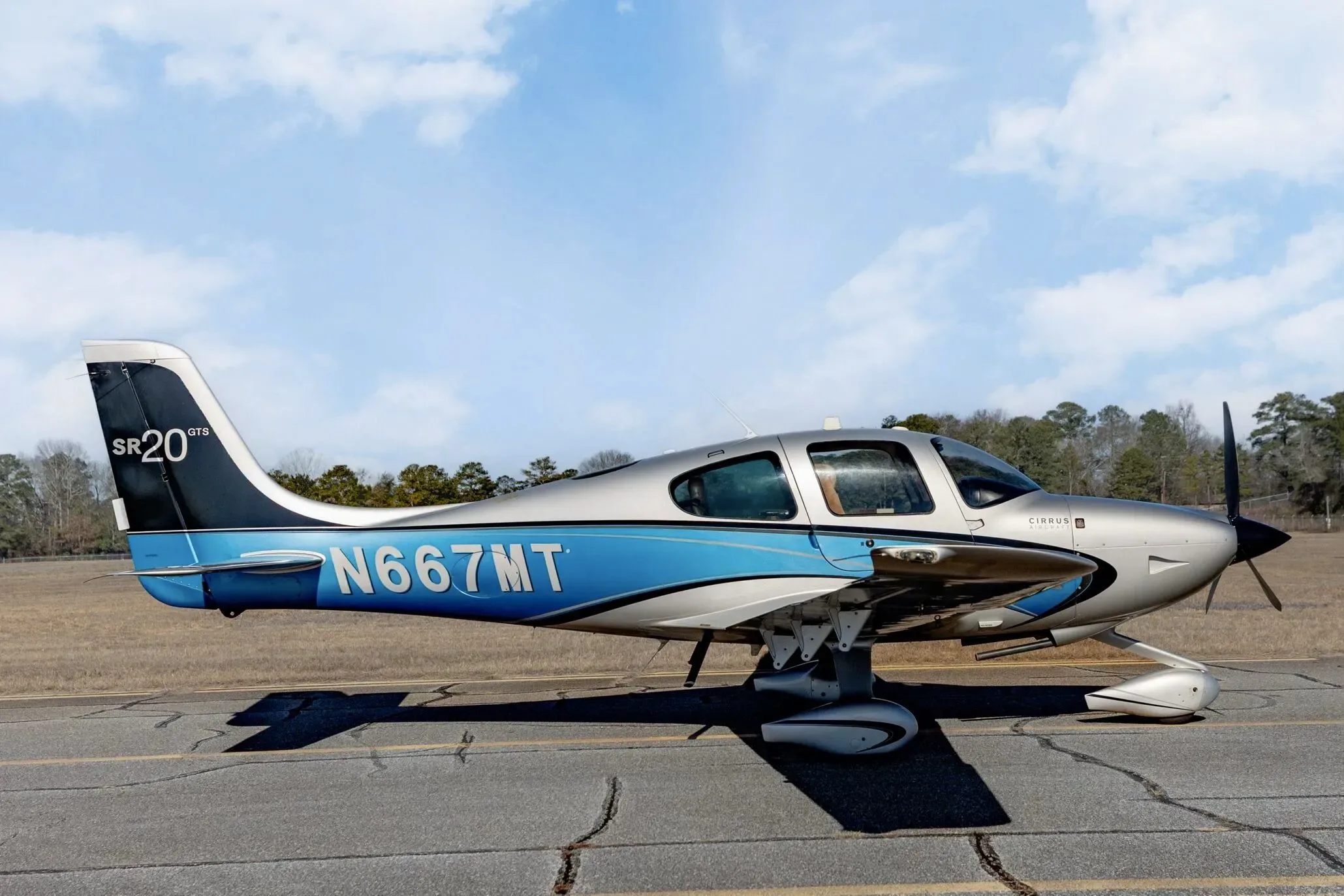 A side view of the Cirrus SR20 GTS aircraft with N667MT registration on an airfield under a partly cloudy sky.
