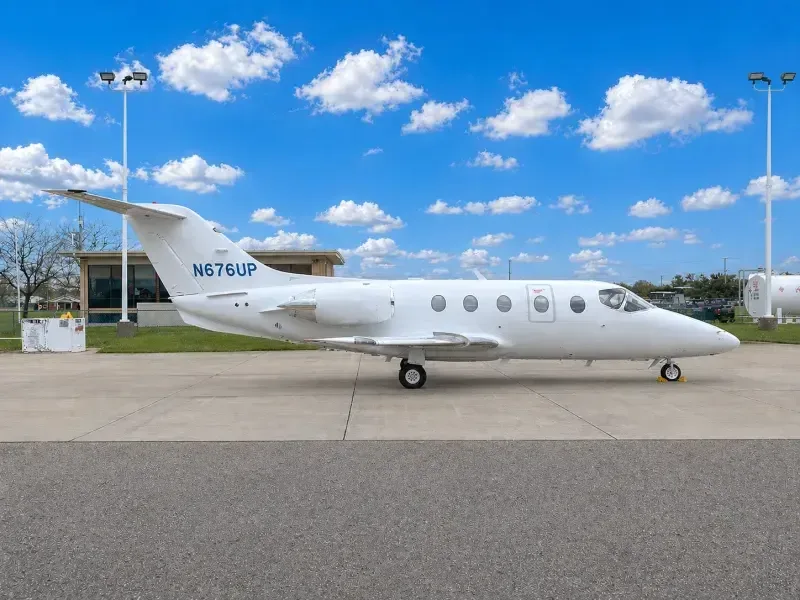 A white business jet, registration N676UP, parked on an airport tarmac under a blue sky with scattered clouds.