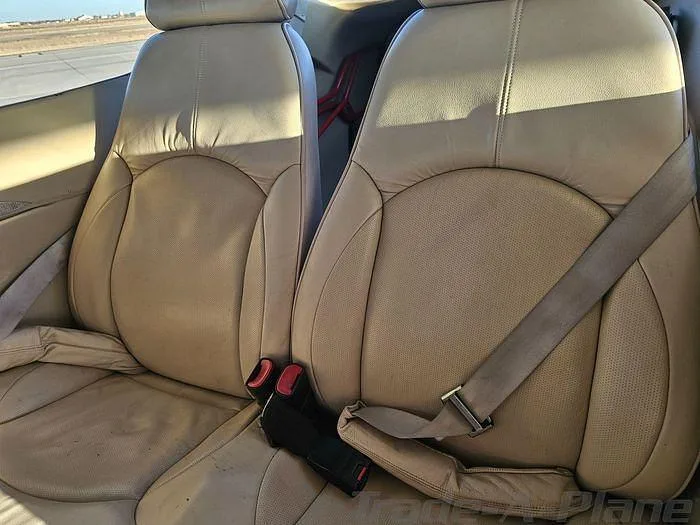 Two light tan leather aircraft seats with seatbelts are shown in the aircraft cabin.