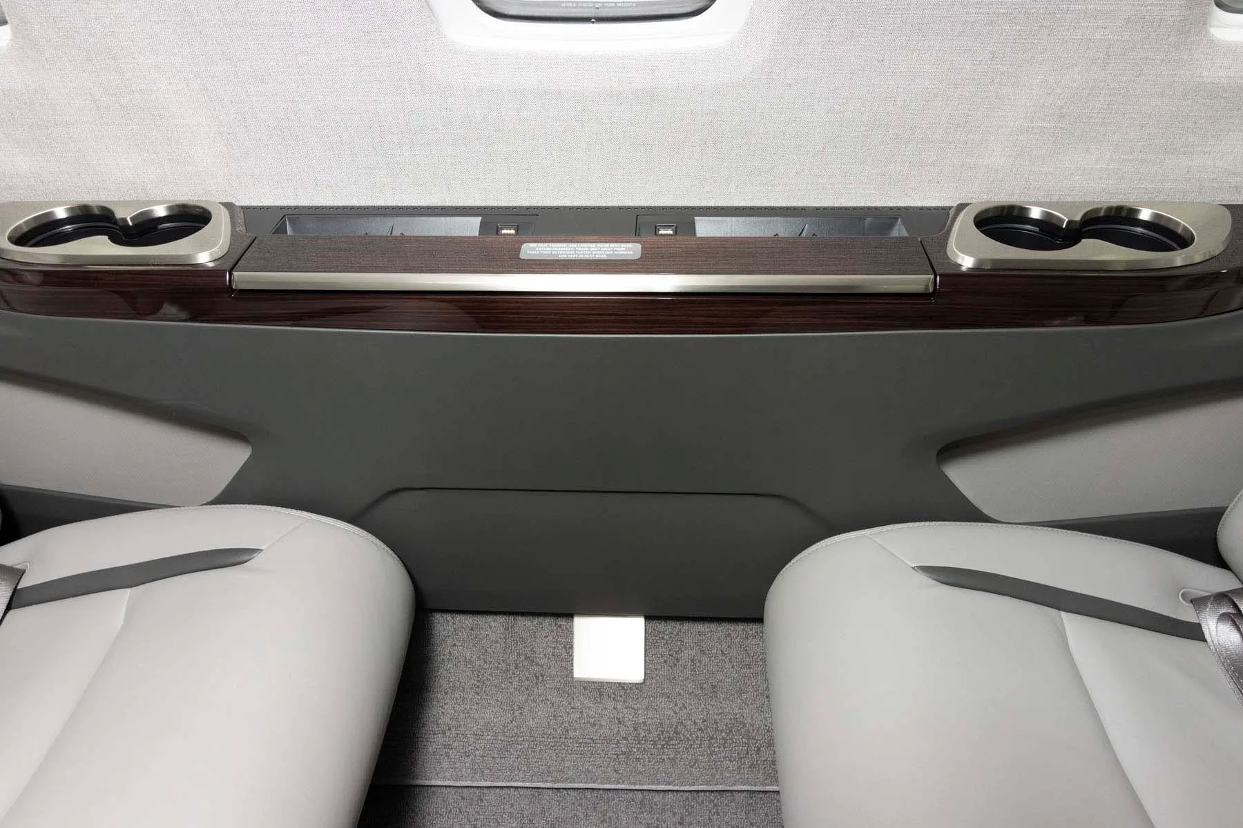 A close-up view of the private jet's cabin side panel with cup holders and a dark wood trim.