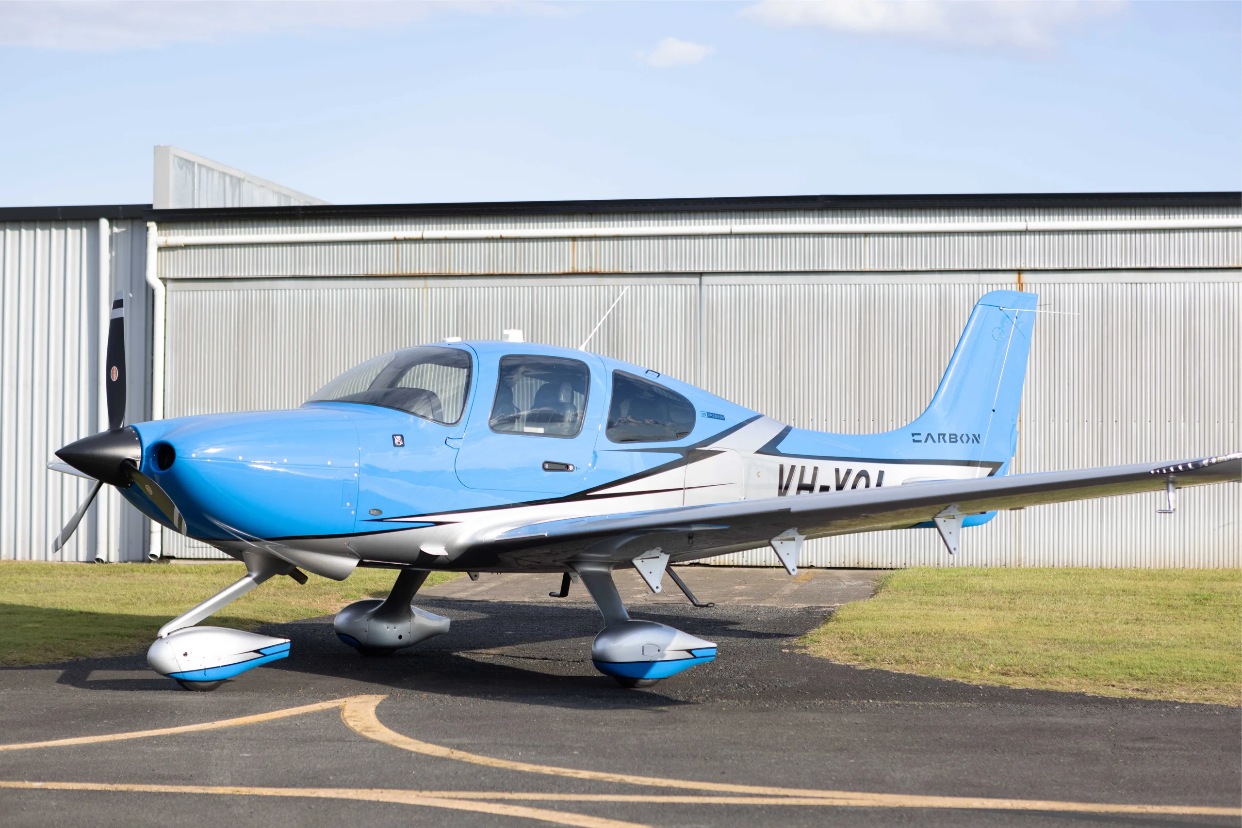 A blue and silver single-engine propeller aircraft, registration VH-VOI, parked on an airfield in front of a hangar.