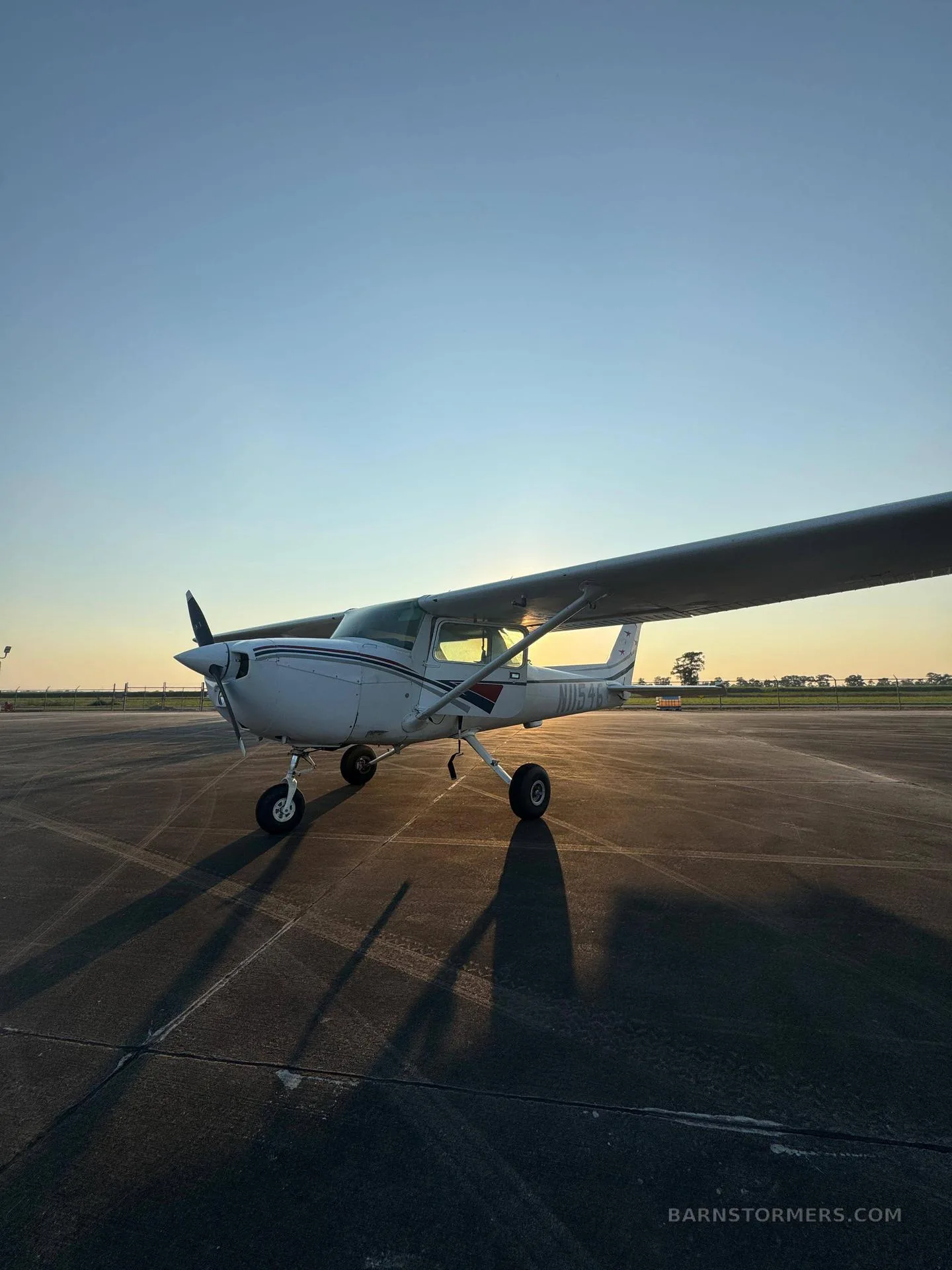 A white Cessna 172 with red and black stripes on the fuselage, parked on an asphalt tarmac at sunset.