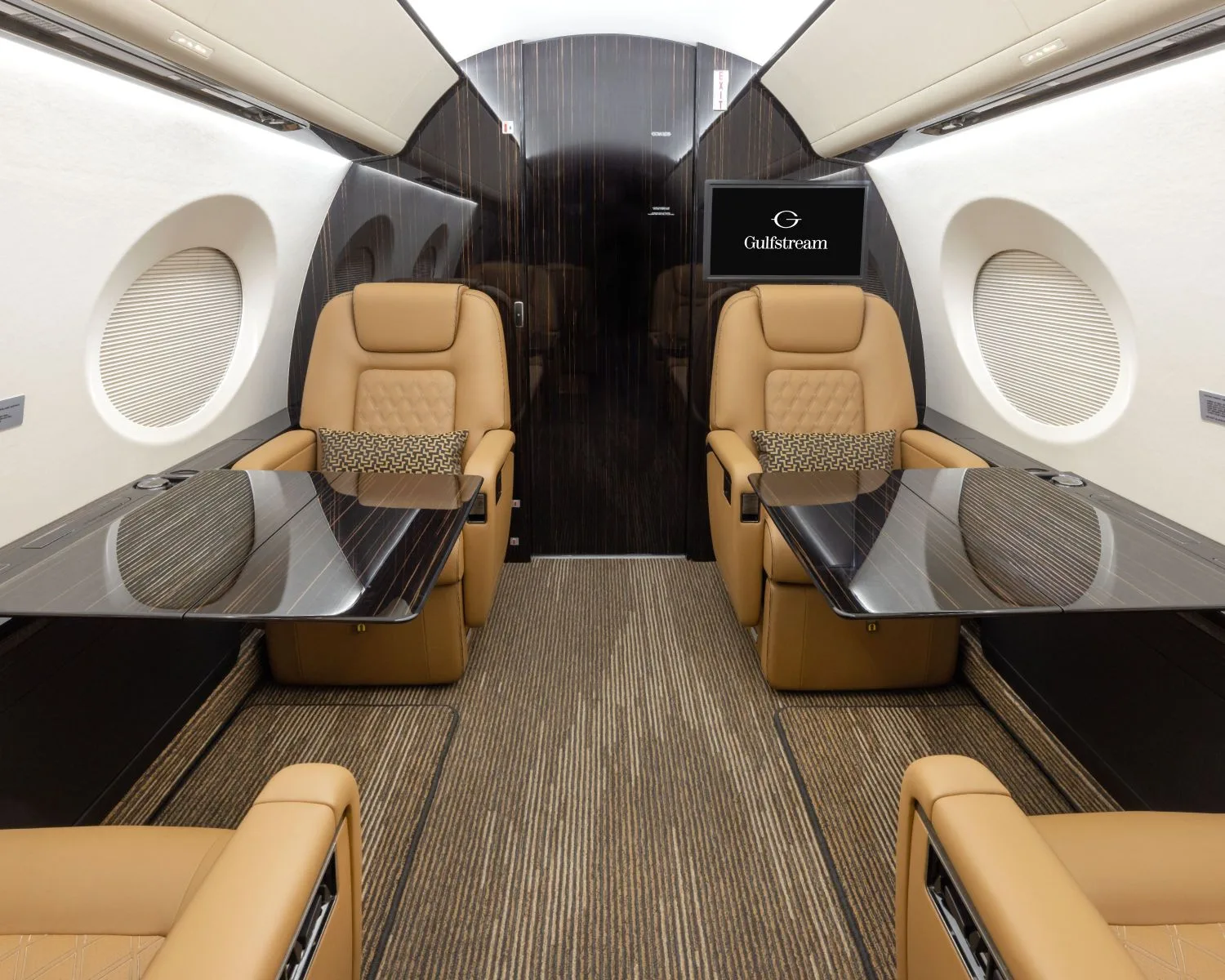 A view of the aircraft's interior with tan leather seats and a dark wood accent wall with tables.
