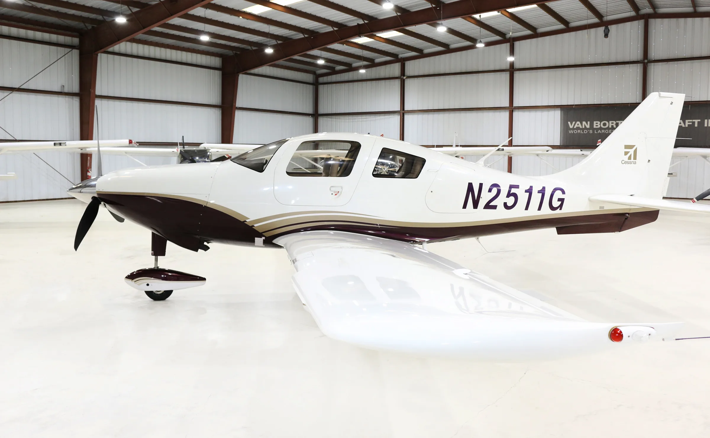 A white and brown single-engine propeller aircraft, N2511G, is parked in a hangar, viewed from the side.