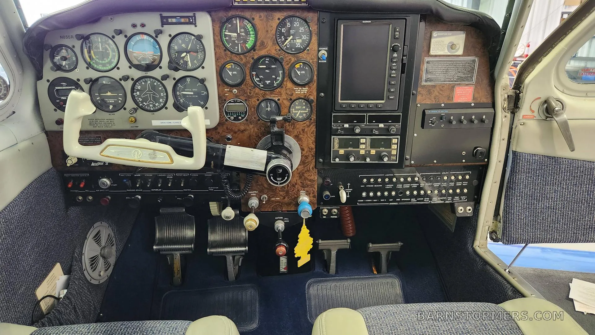 A wide view of an aircraft cockpit, featuring a wood-grain instrument panel, dual yokes, and various gauges and avionics.