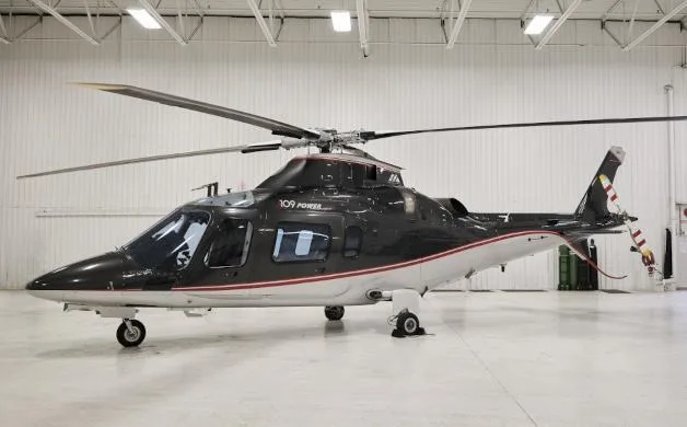 A black and white AgustaWestland AW109 Power helicopter with red pinstripes, parked inside a hangar.