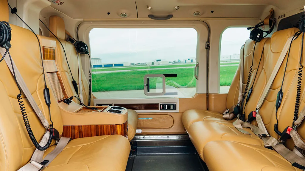 The tan leather interior cabin of the helicopter, showing passenger seats with headsets and a small console.