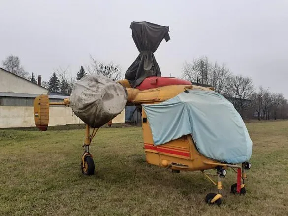 A KAMOV Ka-26 helicopter covered with tarps in a grassy area.