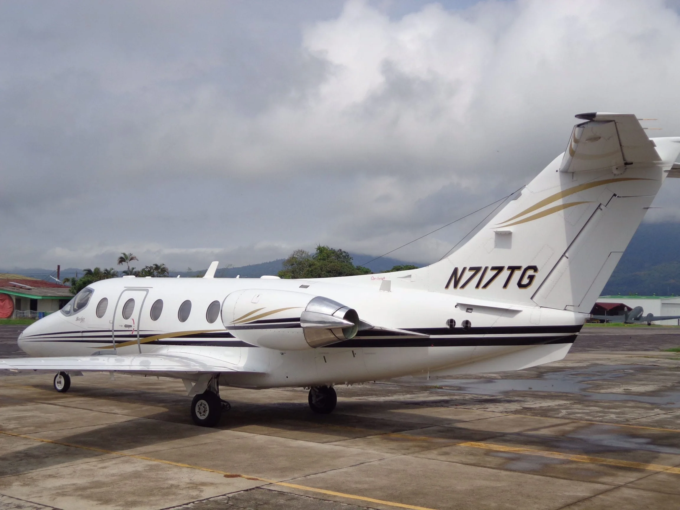 A side view of a white Beechjet 400A with gold and black stripes, registration N717TG, parked on a tarmac.