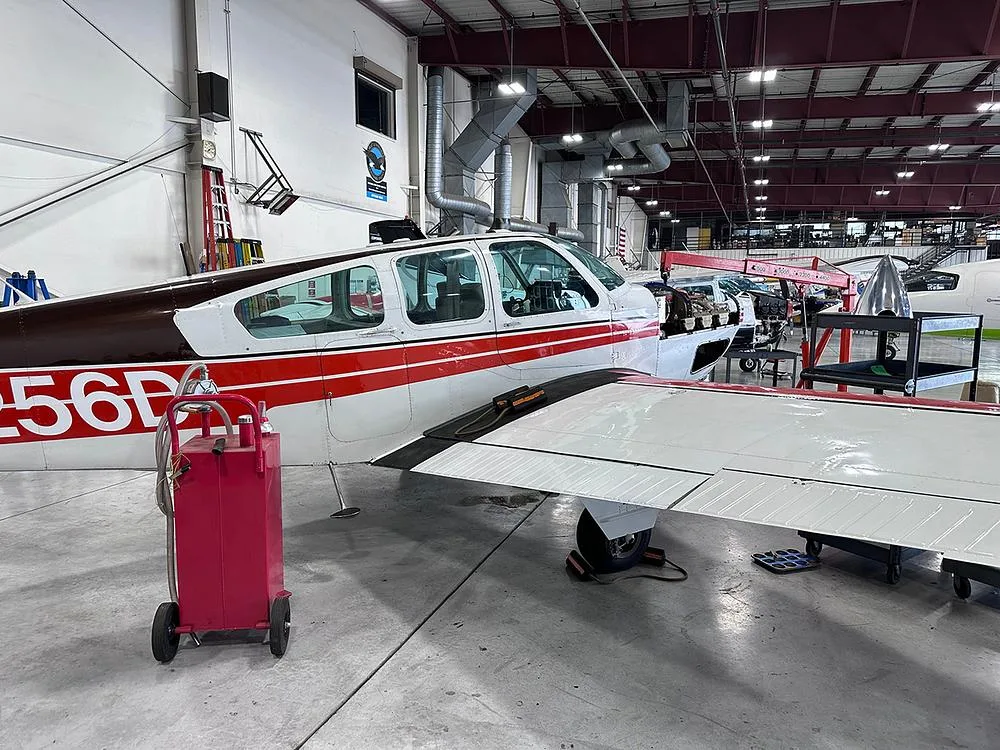 Side view of a white and red aircraft with its engine cowling open, in a hangar with maintenance equipment.