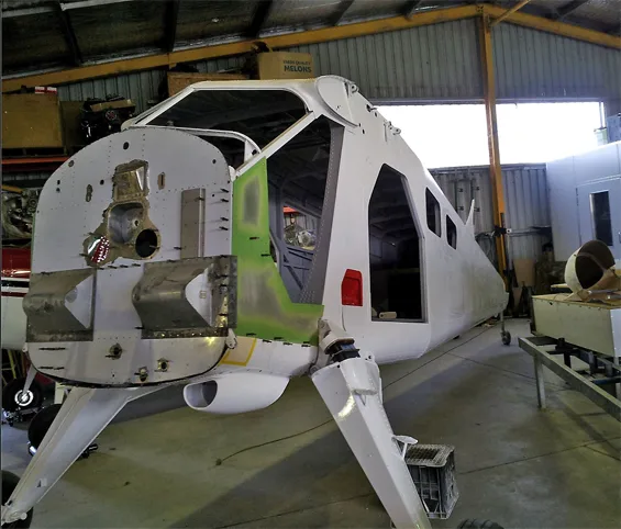 The white fuselage of an aircraft, with its nose section open, in a hangar.