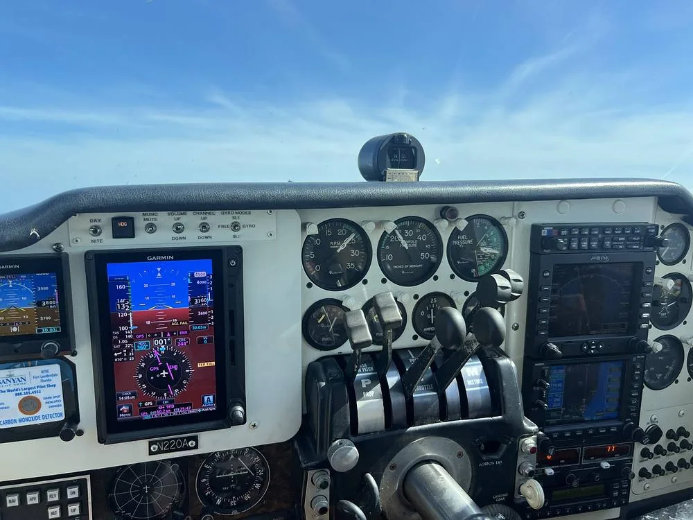 A close-up view of the aircraft's instrument panel, showing multiple analog gauges, digital Garmin displays, and flight controls.