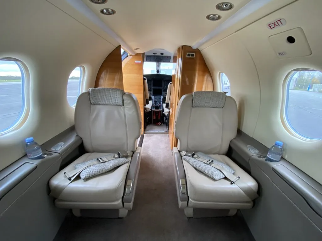 The beige leather interior cabin of an aircraft with two forward-facing seats, with the cockpit visible through the open door.