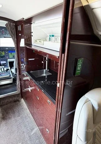 The aircraft's galley area featuring a sink, dark countertops, and wood cabinetry, with the cockpit visible in the background.