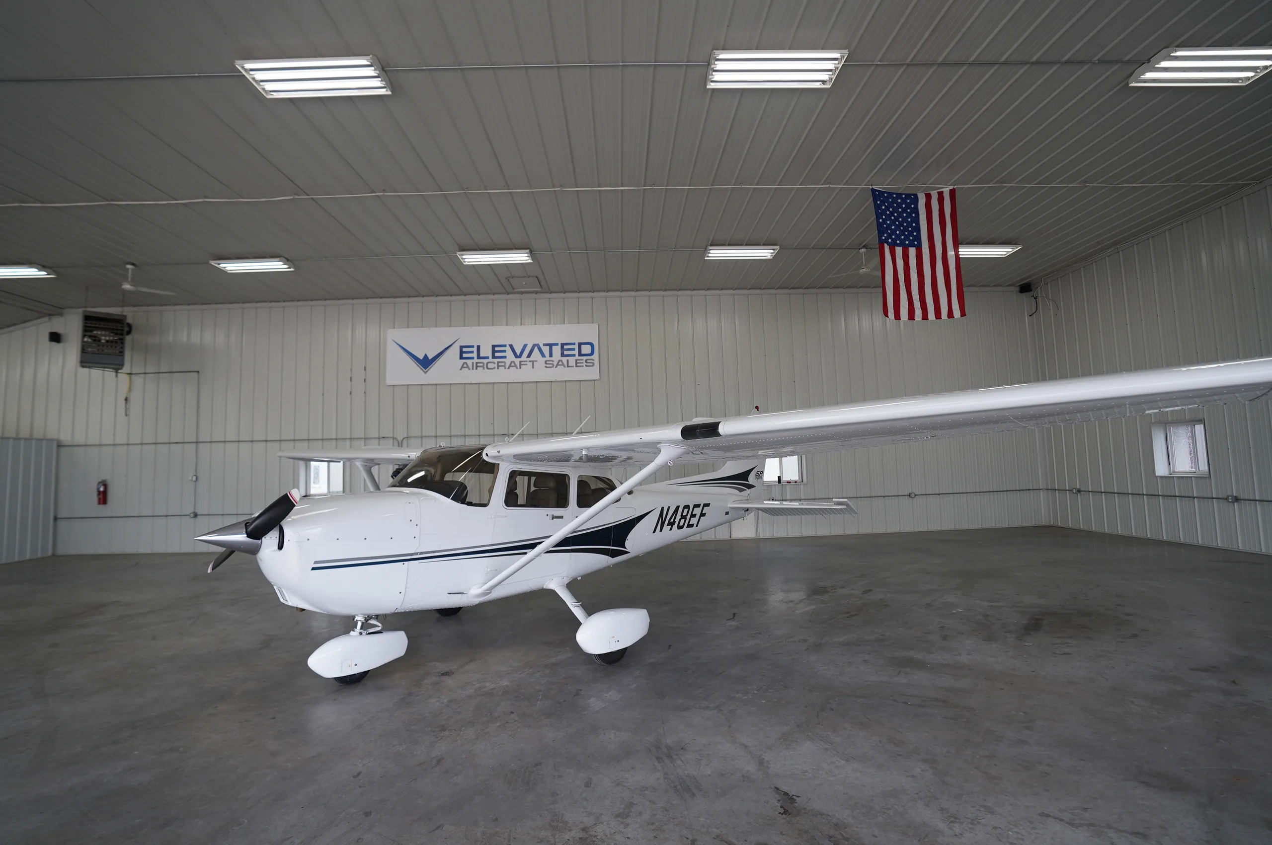 A white Cessna 172 (N48EF) with blue and black stripes parked in a hangar.