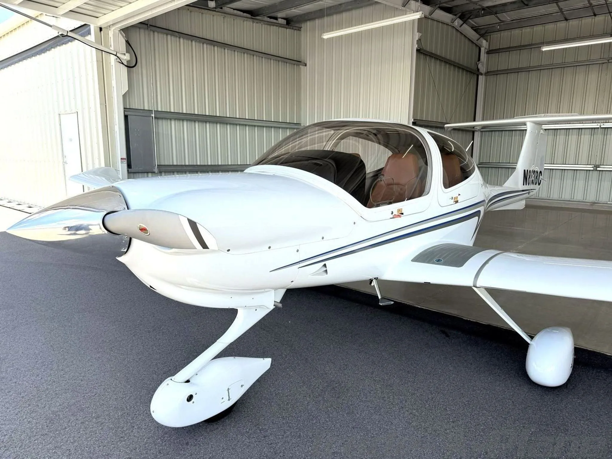 A front-quarter view of a white Diamond Star DA40 XLS aircraft with blue and grey stripes, tail number N853BC, parked in a hangar.