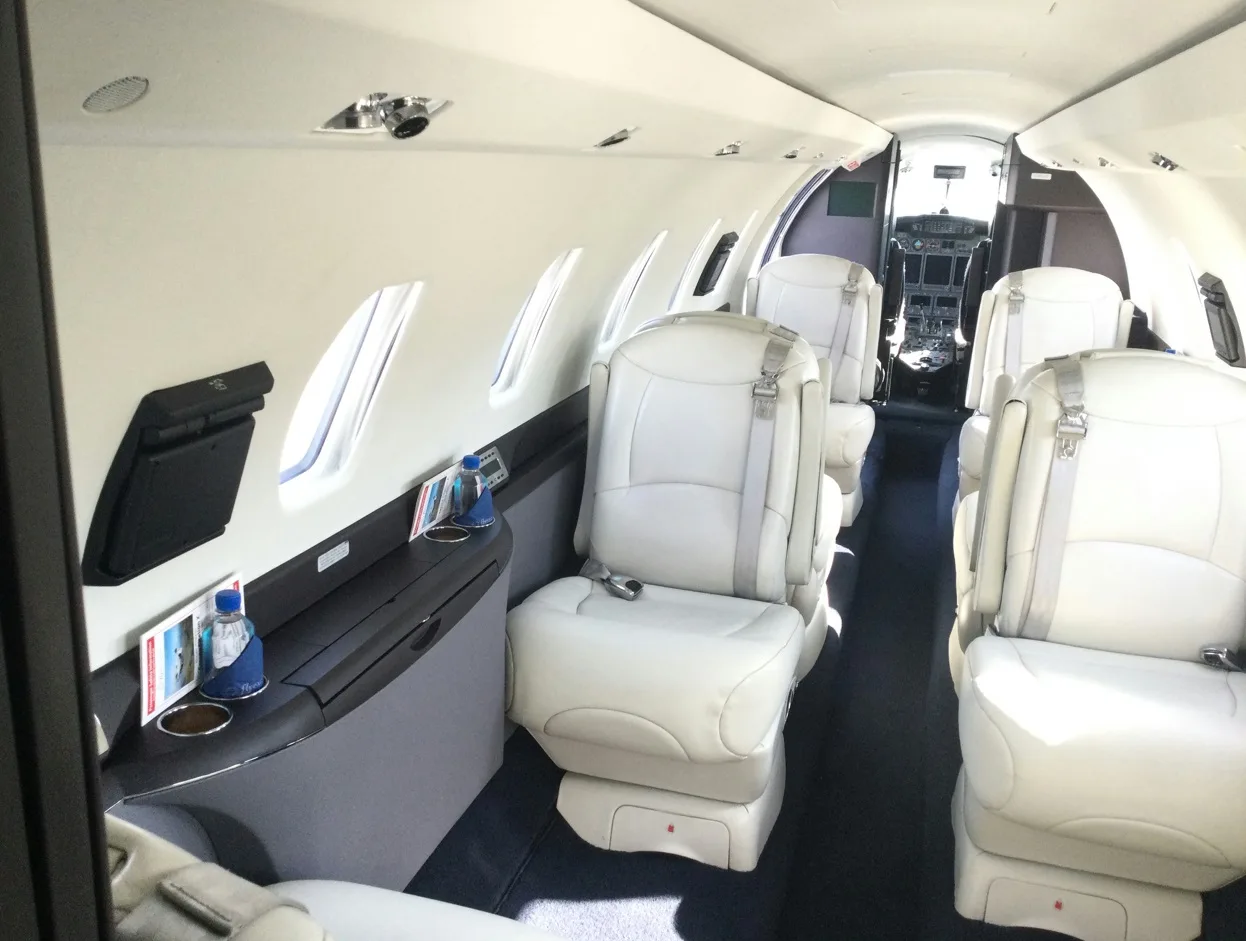 Aircraft cabin with light gray leather seats and a view towards the cockpit.