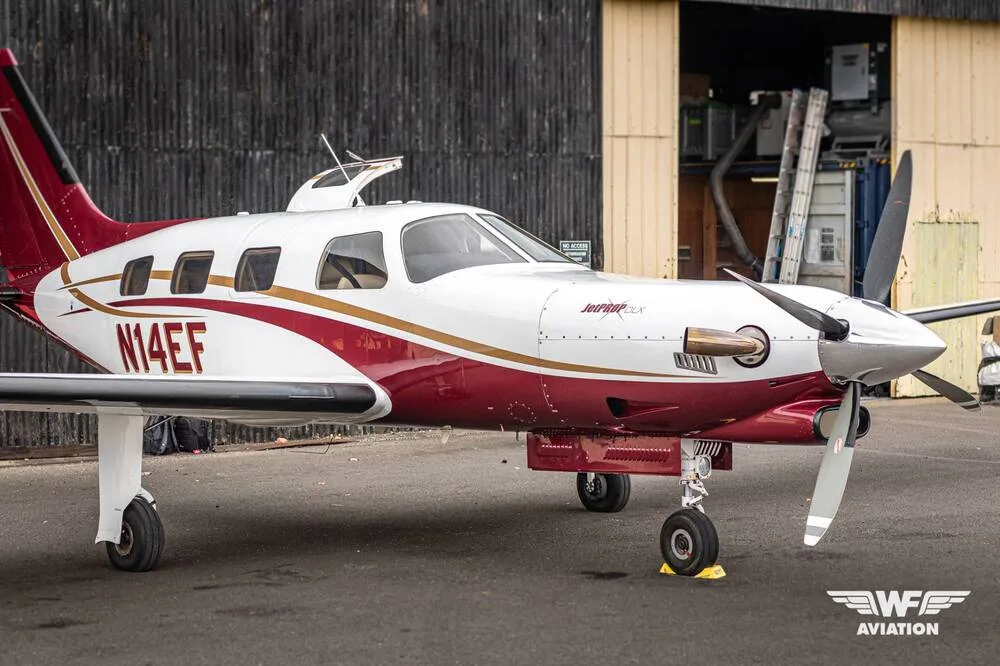 A close-up side view of the N14EF turboprop aircraft, white and maroon with gold trim, parked on a tarmac.