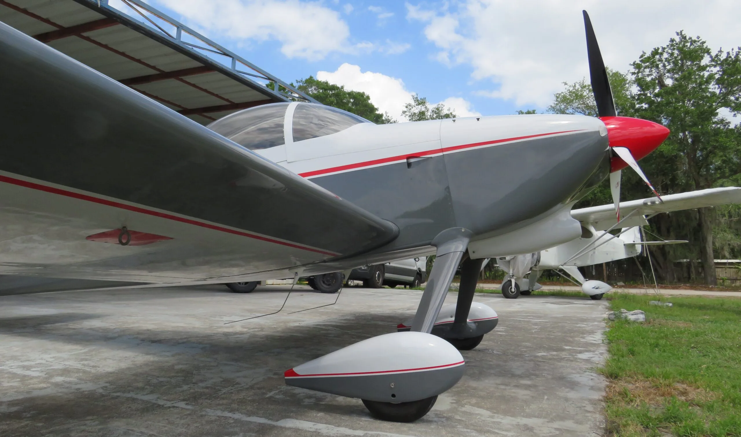 Low-angle view of the front fuselage, wing, and main landing gear of a white and grey aircraft with red accents.